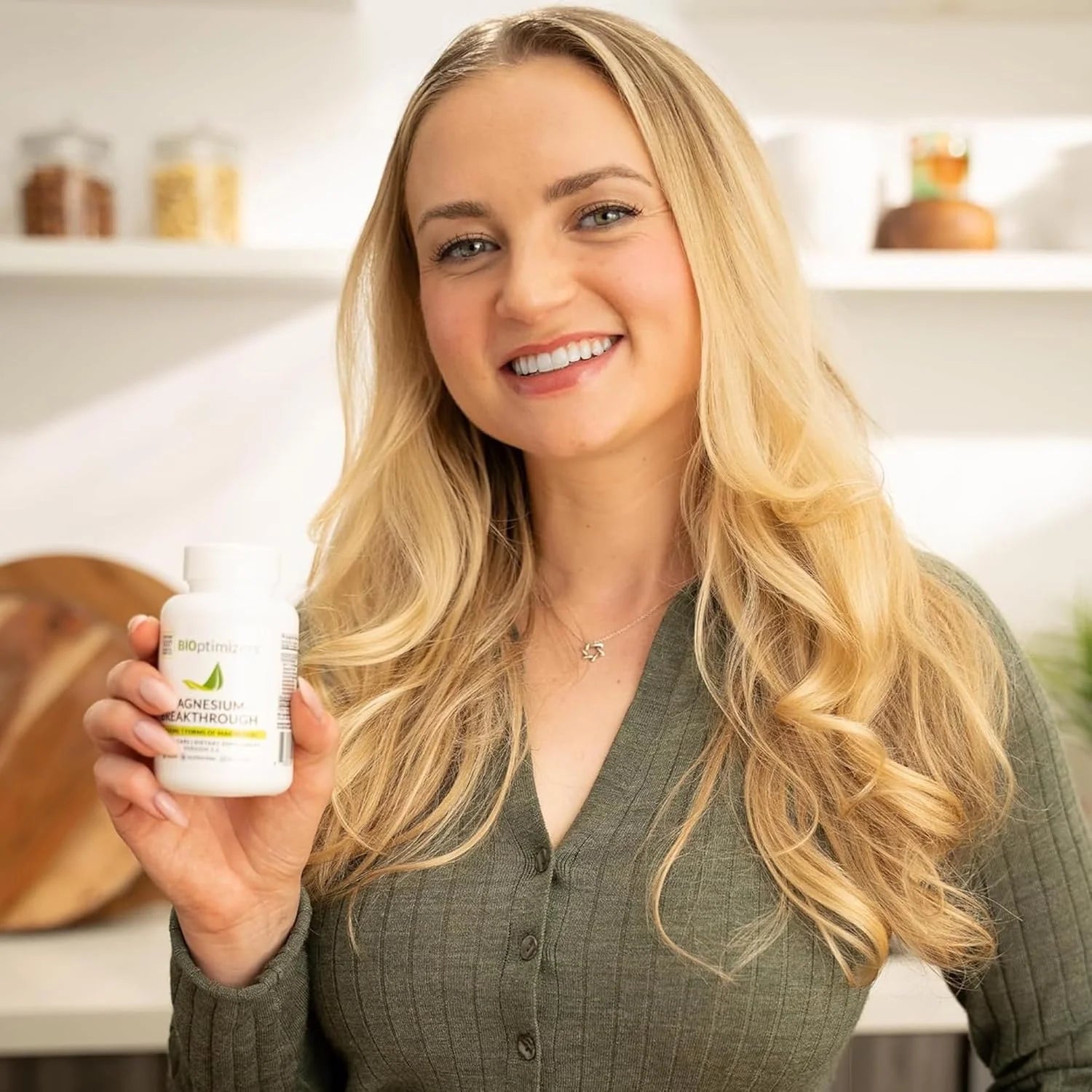 Woman holding a bottle of supplements in a kitchen setting